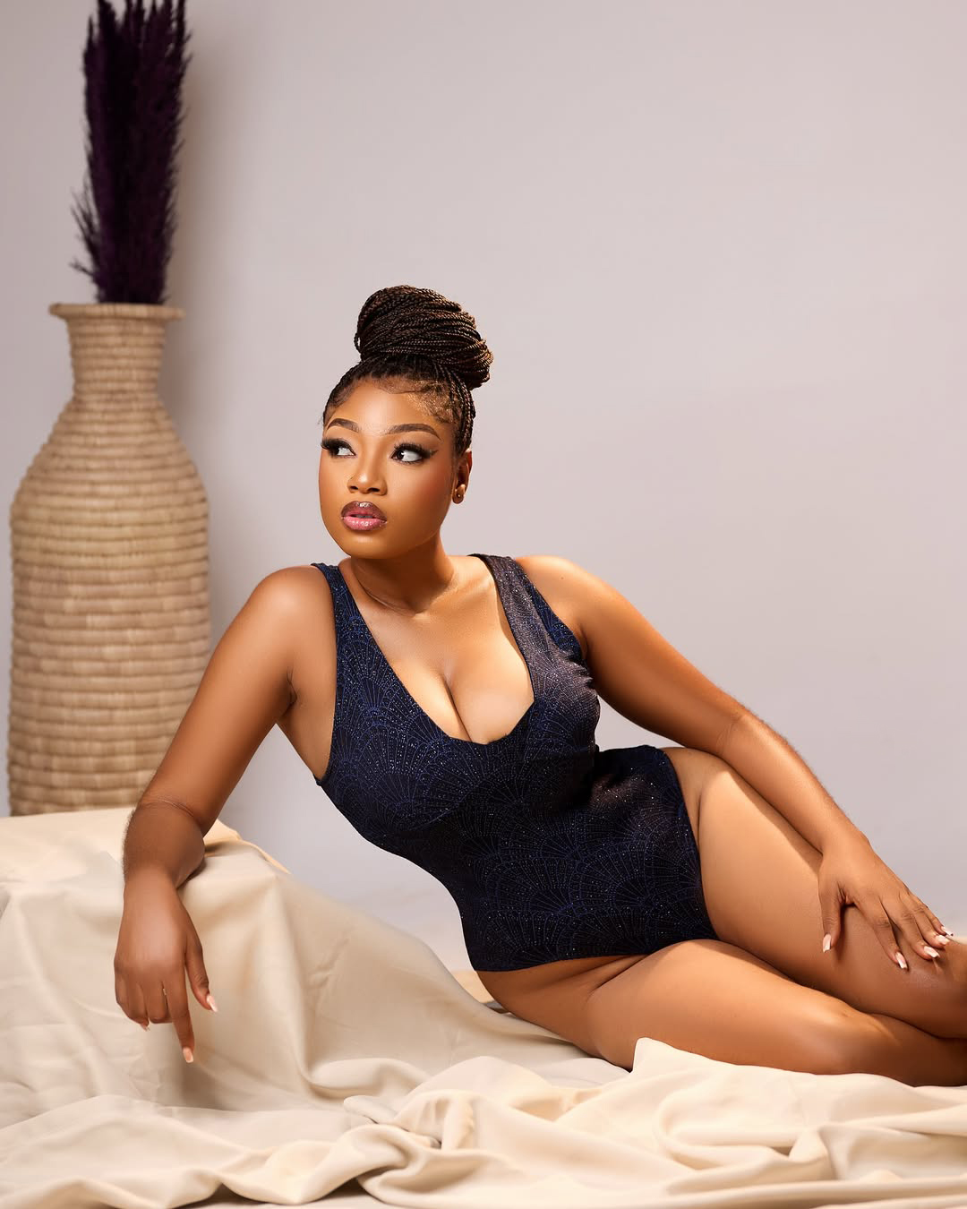 Glamour studio photo of a woman in a black bodysuit posing on white fabric. Portrait by Birdy Images.