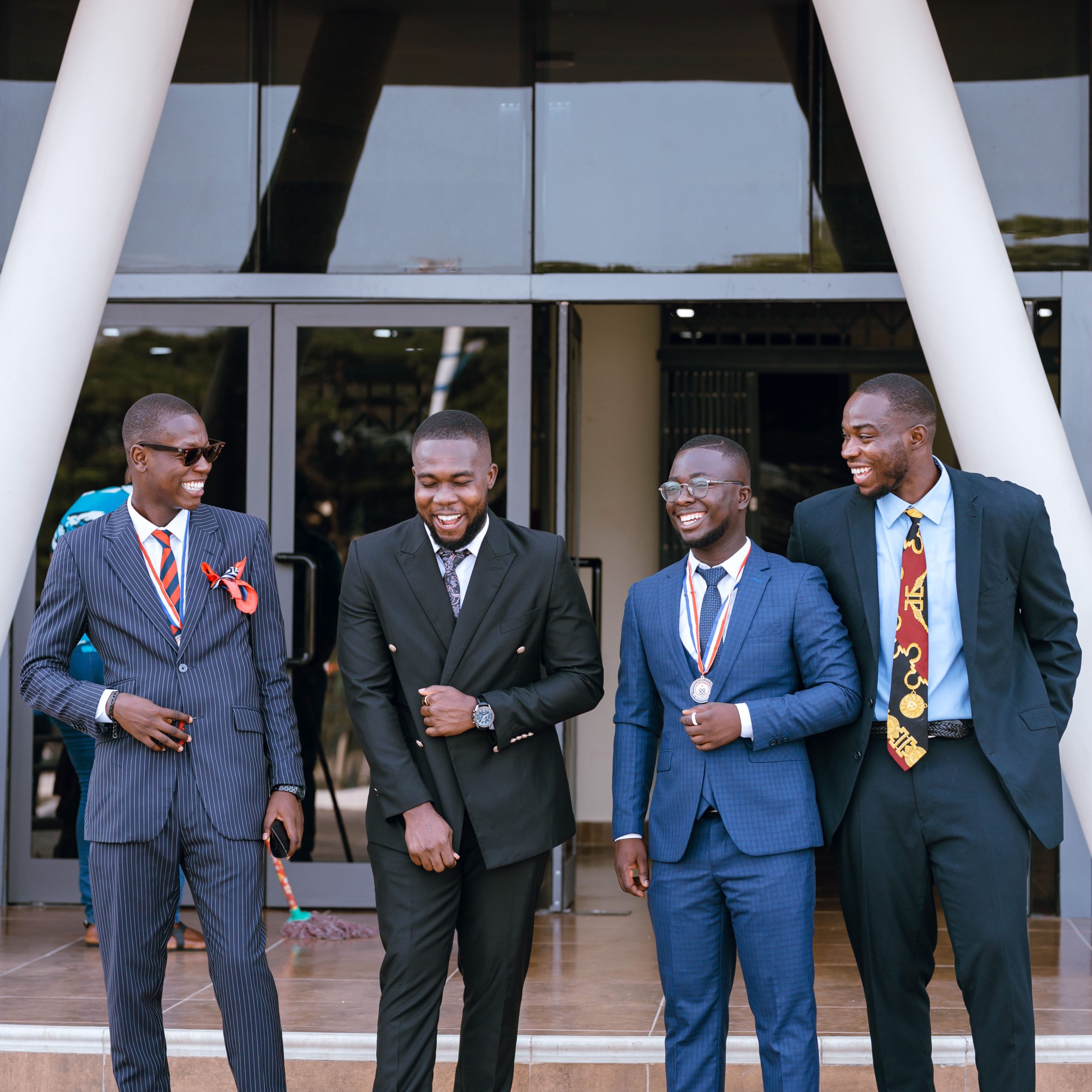 Group og male graduates in professional suits laughing during a grad moment photoshoot at UEW